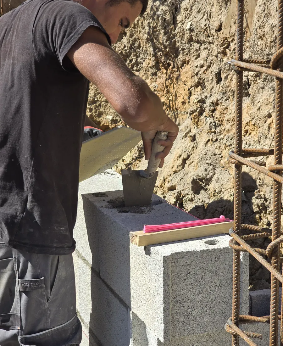 Ouvrier VIANA posant du mortier à la truelle sur un bloc béton